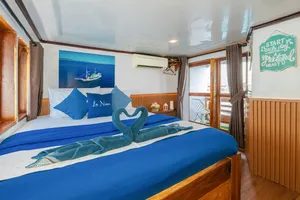 La Famille cabin with blue-and-white bedding, a folded towel lizard and a chalkboard welcome note by the window, Labuan Bajo