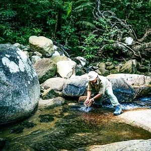 Herbalist-guided gentle forest walk at Gunung Raya, Langkawi with Darulaman Sanctuary: crossing a stream over boulders