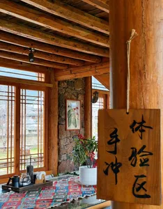 Rustic wooden tea room interior with large pinned calligraphy panel, stone wall and windows, with cups and kettle on a table in Lijiang