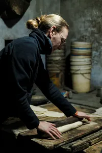 Person flattening and cutting dough on a wooden workbench inside a Hoi An workshop on an early-morning trades ride