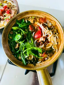 Bowl of steaming Yunnan-style noodle soup with greens, chilli and herbs on a table in Lijiang
