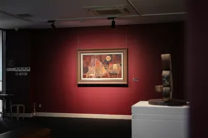 A framed painting on a red gallery wall and a display pedestal inside Quang San Art Museum in Ho Chi Minh City