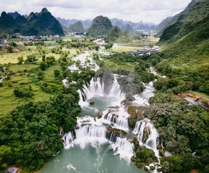 Aerial view of a valley and river with scattered homes, where a broad waterfall cascades through dense green hills