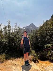 Solo trekker stands on a sunlit path in thick jungle near Mt Fansipan in Sapa, holding trekking poles during the day hike