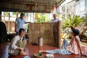 游客与一位主理人在会安一间明亮的竹屋里,坐在垫子上参加动手工作坊,屋内有花园植物点缀。