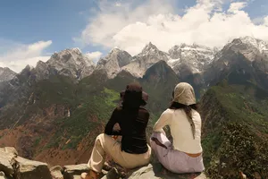 Two travellers sitting on a cliff watching the snow-dusted peaks of Tiger Leaping Gorge, Lijiang, on the 2D1N high trail