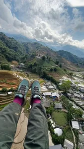 Paragliding passenger view over terraced rice valleys and mountain village paths far below, with clouds overhead, above Vietnam's Sapa