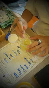 Close-up of hands adding fragrance to a small container above handwritten scent labels for a Singapore candle workshop