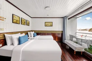 Halong Bay party cruise cabin with neatly made beds, blue pillows and dark wood floors, plus an open door to the deck