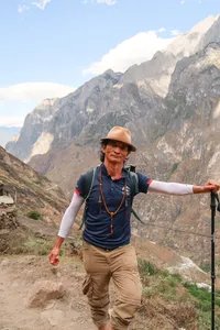 Trek leader in a wide-brim hat guiding hikers along a mountain slope on the high trail of Tiger Leaping Gorge in Lijiang, with The Bivou Lijiang