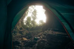 Tent interior opening to sunlit forest beyond, with cave camp gear on the ground inside Phong Nha-Kẻ Bàng during a Greenland Tours trip