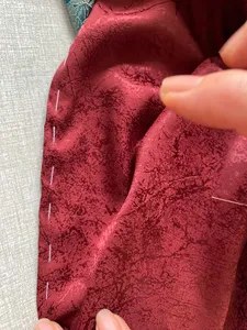 Close-up of hands holding maroon patterned fabric while working on a craft project in a Hanoi Red River village