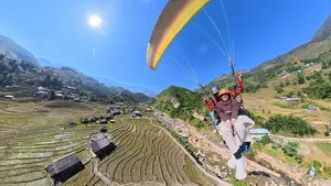 Paragliding above tiered rice terraces with a pilot guiding a passenger over green valleys and mountains in Sapa