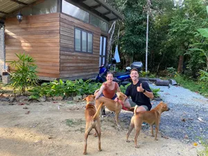 People relaxing with several dogs in front of a wooden cabin amid greenery at Kebun Lidstari permaculture farmstay in Langkawi