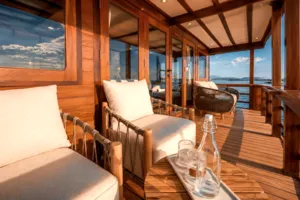 Wooden phinisi deck lounge with beige armchairs, a small table and sea view, during a Komodo group cruise in Labuan Bajo