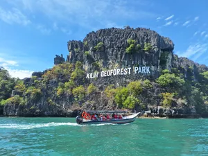 Speedboat with passengers cruising turquoise waters toward the limestone wall of Kilim Geoforest Park, Langkawi with Dev's Adventure Tours