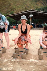 Squatting participant sets coral plugs into concrete bases on a beach restoration site with Rinca Coral Nursery Program in Labuan Bajo