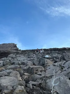 Hikers crouch on Mount Agung’s rocky summit ridge under a bright blue dawn sky during a private sunrise trek with local guides