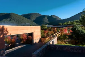 Halaman Linden Centre di eco-retreat Shaxi, Dali, dengan bangunan batu, pepohonan musim gugur, dan pegunungan saat senja