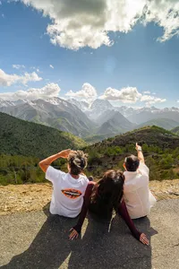 Travellers with arms raised at a high mountain overlook over the Shangri-La valley during a 6-day loop trek