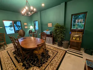 Dining room with a wooden table and chairs, green walls and windows framing the sea at The Unexpected’s Singapore farmstay by the sea