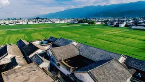 Pemandangan udara rumah-rumah beratap genting di pekan lama Xizhou, Dali, dikelilingi kehijauan sawah dan banjaran gunung di kejauhan