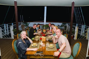 Group dinner on the open-air deck of a Cat Ba cruise boat with shared plates and drinks under evening lights