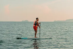 Stand-up paddleboarder on calm sea at sunset with distant islands near Kota Kinabalu