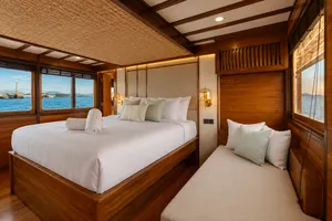 Travass Life phinisi cabin with a double bed, lounge seating and sea-window views for a Komodo shared trip, Labuan Bajo