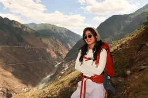 Smiling hiker in sunglasses with a red backpack on the cliff path above Tiger Leaping Gorge in Lijiang with The Bivou Lijiang