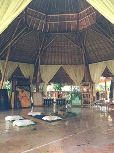 Meditation hall with mats and white hanging drapes beneath a vaulted bamboo roof at Omunity Bali in Bali