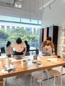 Pottery participants painting glazed ceramic pieces at Ina Atelier studio tables under large windows during workshops in Singapore