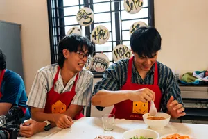 在会安的 Jolie 烹饪课上，围着围裙的客人们在桌边准备食物，碗和食材都已备好