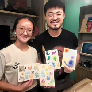 Art For Good art therapy in Singapore: two participants smiling while holding cat-themed paintings during workshops in Singapore