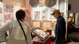 Ho Chi Minh City cultural display: an older host and visitor browse lion dance documents, photos and framed certificates