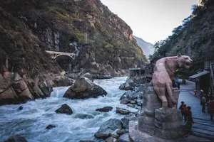 Rocky river gorge in China with fast-flowing water, a riverside walkway, and a large stone animal statue