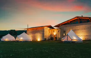 Tents lit by dusk beside stone buildings at a Tibetan mountain valley camp at Shangri-La with Ferme Liotard