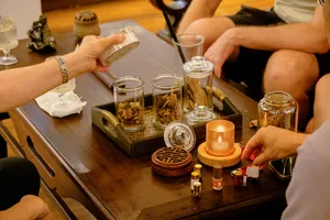 Hands selecting small glass vials on a tasting tray at the Rare Agarwood Tour in Hanoi, with scent samples and cups arranged nearby
