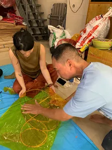 Artisan and guest tying lines on a green lantern frame on a worktable during a lantern-making workshop in Ho Chi Minh City