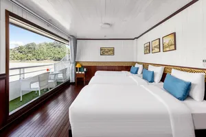 Halong Bay party cruise cabin with a double bed, blue cushions, and large windows showing the lake view outside