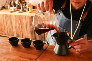 A taster pours dark coffee into a small server for a cupping at the family-run specialty coffee workshop in Lijiang