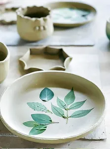 Green-leaf painted ceramic plate on a worktable in Ilham Ceramic Studio, Langkawi, with other bowls blurred behind