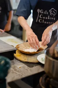 Hands pressing dough in a woven tray at a Gili T cooking class in Lombok, with Gili Cooking Classes aprons