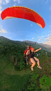 Paragliding passengers float together beneath an orange canopy above forested slopes and distant mountains in Sapa