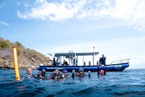 Divers bobbing in the sea beside a dive boat during Lombok Pink Beach 2 Fun Dives in Lombok under a bright sky