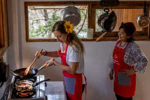 Host-led forage-to-table cooking class in Mae Kampong, Chiang Mai: cook stirs a pan while another instructor watches in a kitchen