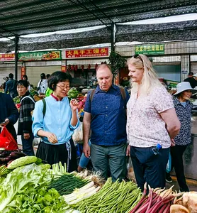 A Yunnan cooking host guides travellers through a morning market in Lijiang, pointing out fresh greens and herbs at stalls