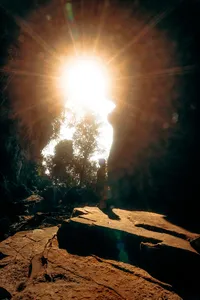 Traveller silhouetted at the mouth of a Phong Nha cave as bright sunlight streams in, with rays filtering into the darkness