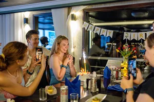 Birthday party on the Oasis Bay Party Cruiser with friends at a candlelit table, celebrating together on Halong Bay