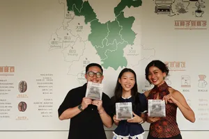 Tasting participants hold up Yunnan coffee sample bags in front of a map wall during a specialty workshop in Lijiang